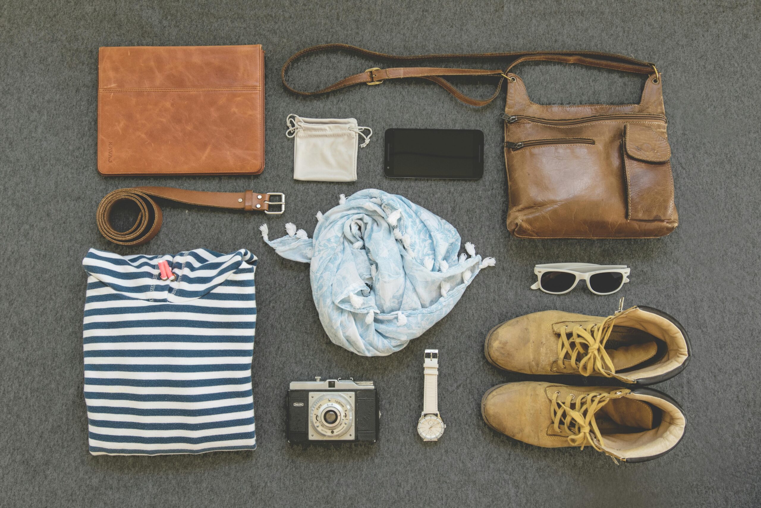 Travel accessories such as headphones, passport holder, and neck pillow near a stylish expandable weekender bag