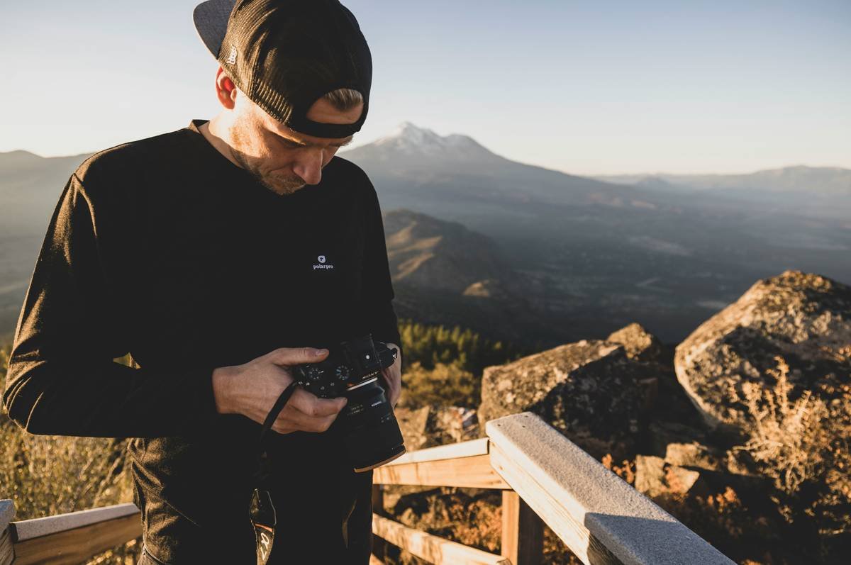 A sleek black expandable suitcase with wheels, showing its expanded state next to a pile of clothes and accessories