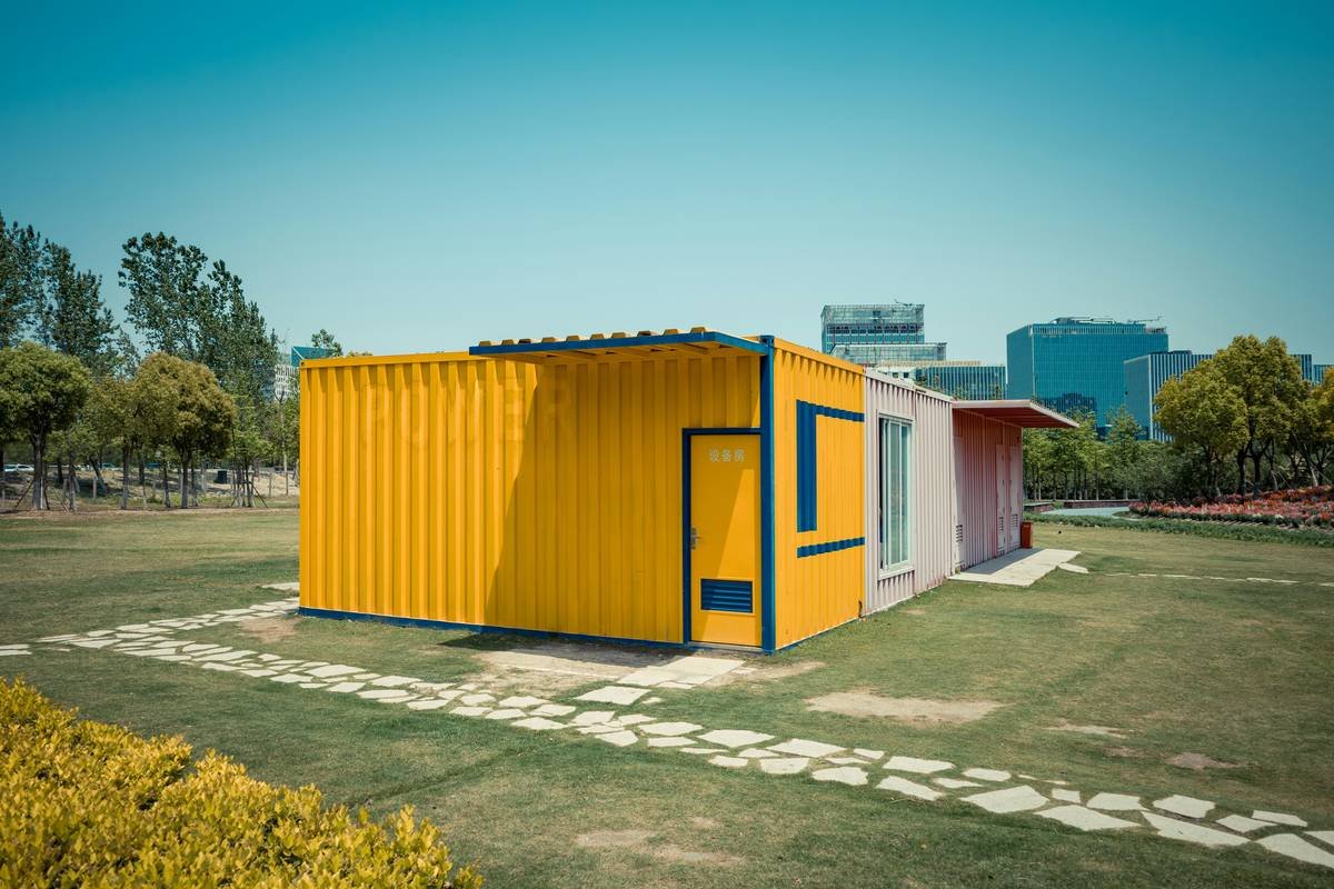 A bright yellow shipping container home on a green lawn.