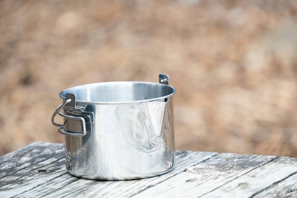 A shiny metal pot with a handle sits on wood.