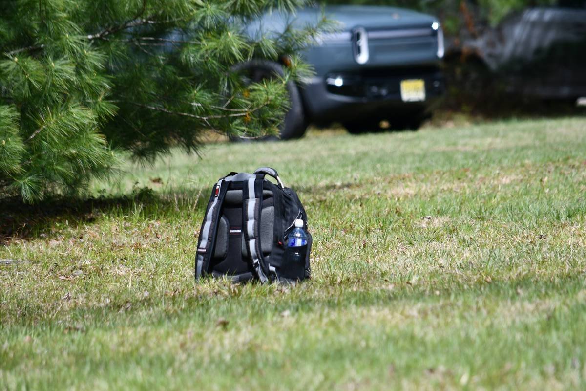 Black backpack with water bottle on grass near a car.