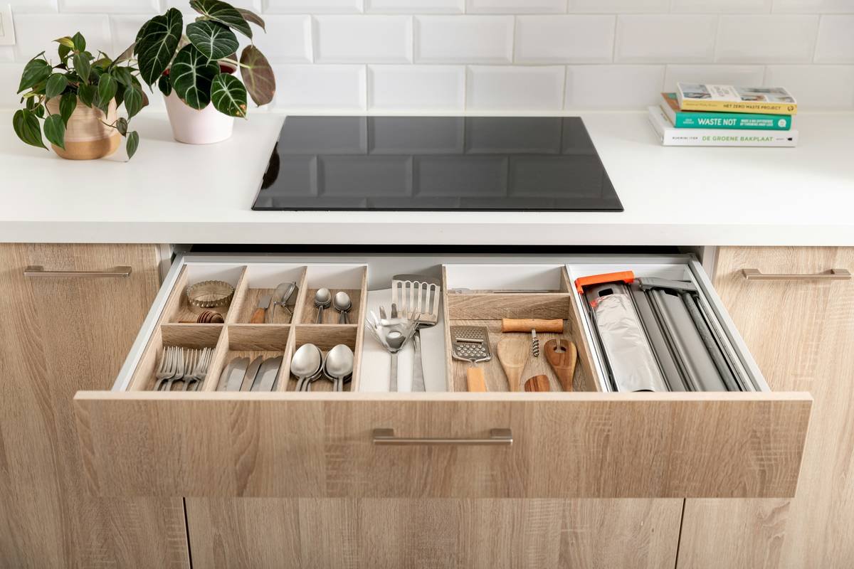 Cutlery drawer in a wooden and white kitchen with wooden drawer inserts.