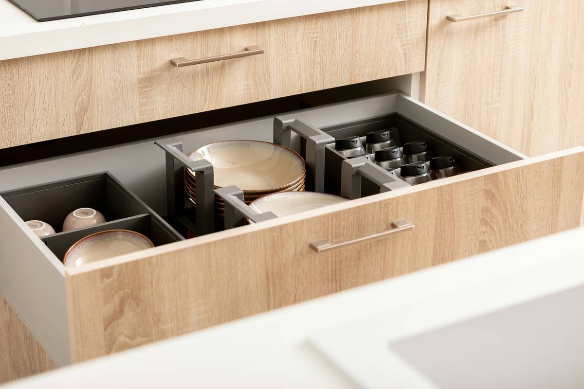 Organized kitchen drawer with plates, spices and cups in drawer organizers.